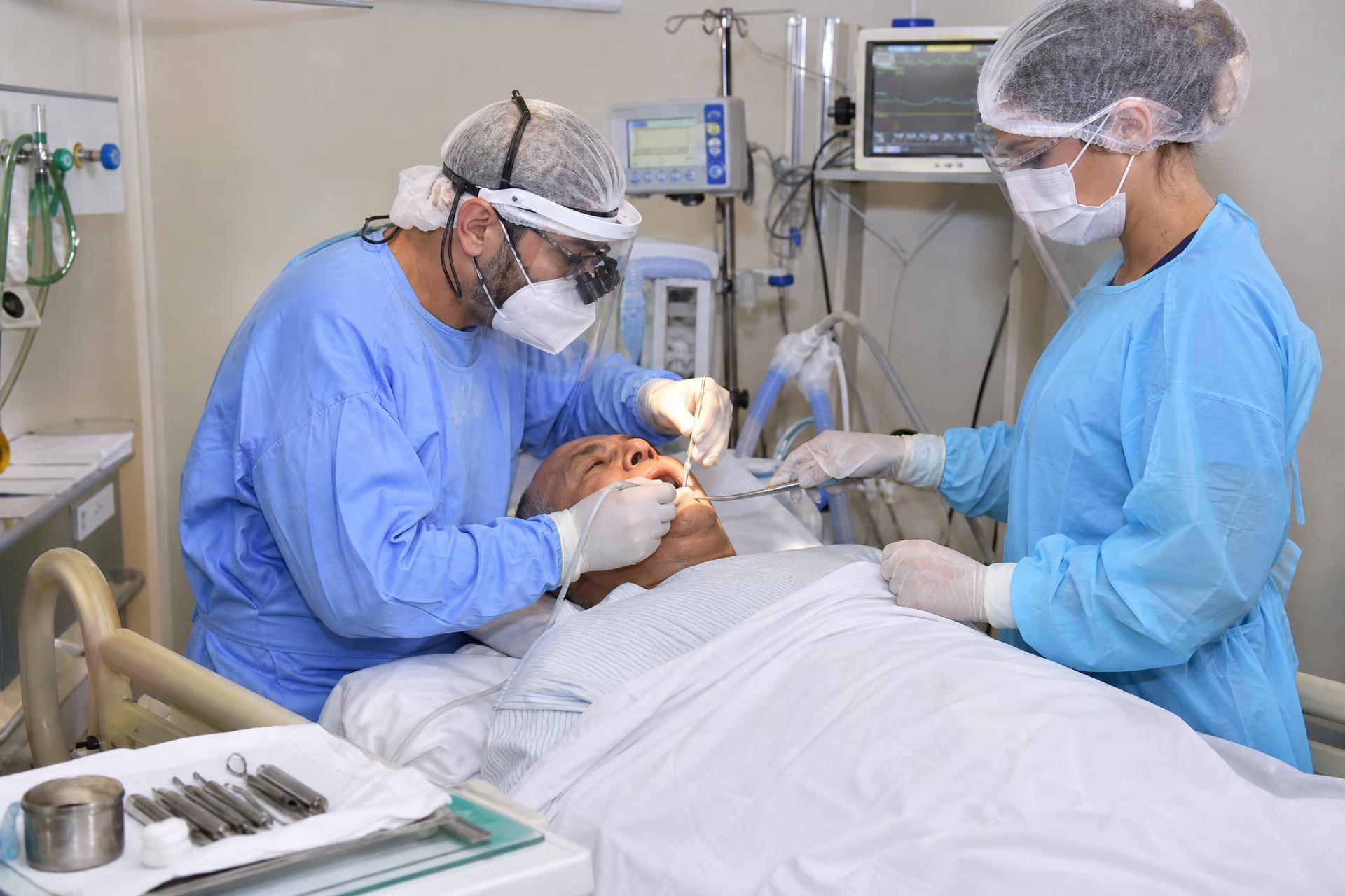 Dentista atendendo paciente em leito de UTI hospitalar